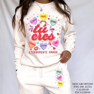 May include: A white sweatshirt with a graphic design of colorful hearts with Spanish text that reads "tu eres" and "eternamente amada".
