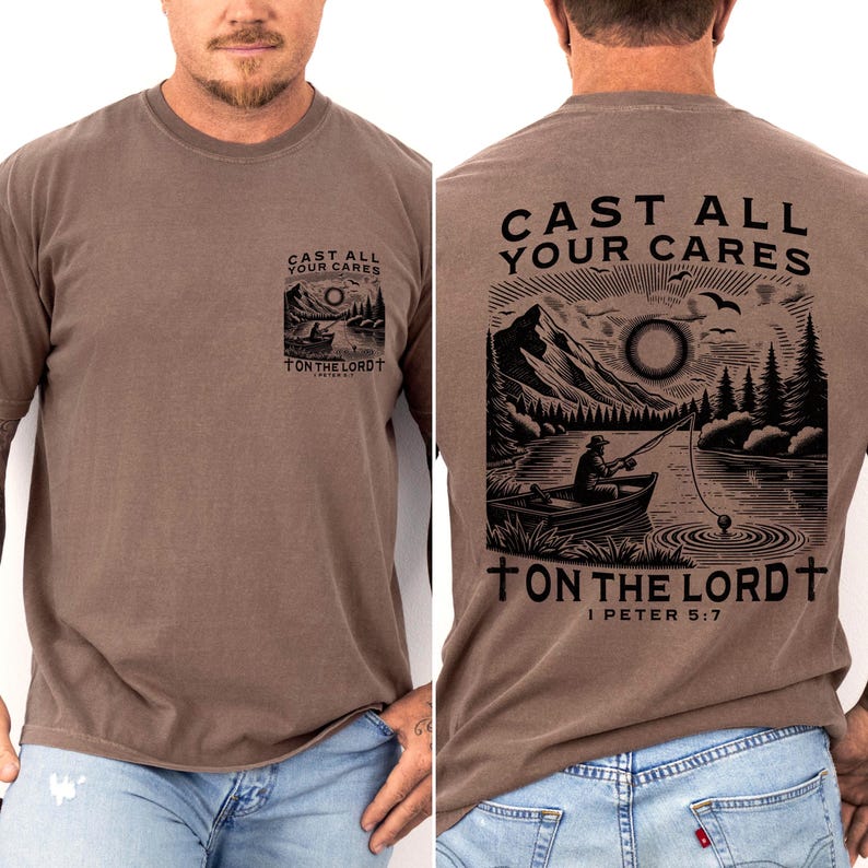May include: A brown t-shirt with a graphic on the front and back. The front graphic is a small square with a lake scene and the text 'CAST ALL YOUR CARES ON THE LORD'. The back graphic is a larger lake scene with a person fishing and the text 'CAST ALL YOUR CARES ON THE LORD I PETER 5:7'.
