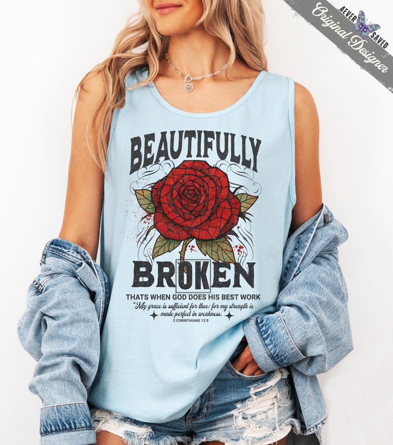 May include: Light blue tank top with the words "BEAUTIFULLY BROKEN" in black, featuring a red rose graphic. The text "THATS WHEN GOD DOES HIS BEST WORK" and a Bible verse are also printed on the shirt.