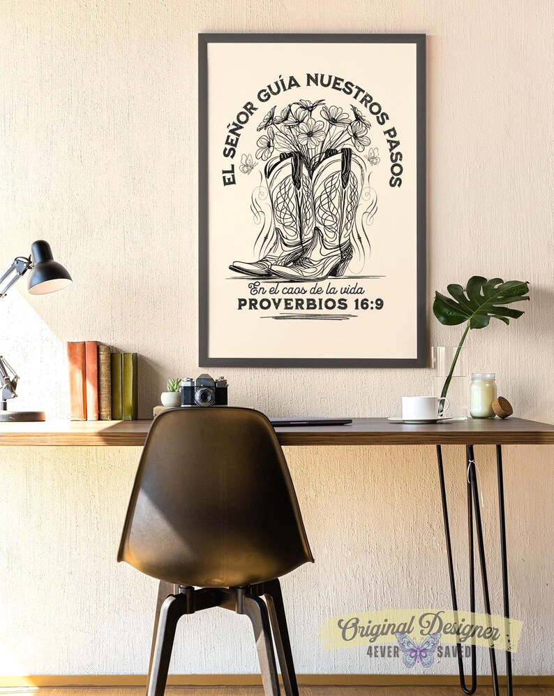 May include: A framed black and white print featuring cowboy boots filled with flowers. The text reads "EL SE&Ntilde;OR GU&Iacute;A NUESTROS PASOS" and "En el caos de la vida PROVERBIOS 16:9". The print is displayed on a wall above a desk with a chair.