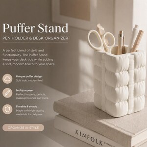 Puede incluir: Organizador de escritorio y portalápices Puffer Stand de color crema. El soporte tiene un diseño acolchado único y suave y contiene bolígrafos, lápices y tijeras. El texto "Puffer Stand" y "Organize in Style" son visibles.