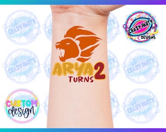 May include: A temporary tattoo with an orange lion head and the text "ARYA 2 TURNS" in yellow, red, and orange. The tattoo is on a person's wrist.