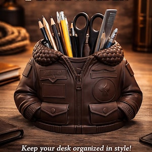 Puede incluir: Un portalápices marrón con forma de chaqueta lleno de lápices, bolígrafos y tijeras. El texto "JACKET PENCIL HOLDER" está en la parte superior. La parte inferior de la imagen dice "Keep your desk organized in style!" con las palabras "Unique Gift", "Handcrafted" y "Cool Desk Decor".