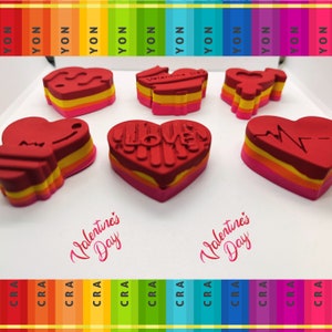 Puede incluir: Seis sellos de goma en forma de corazón rojo con diferentes diseños. Los sellos están superpuestos en rosa, naranja y amarillo. Los sellos están dispuestos sobre una superficie blanca. El texto "Valentine's Day" está escrito en rosa sobre la superficie.