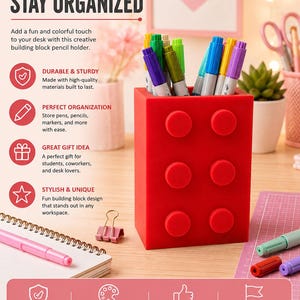 Puede incluir: Un portalápices rectangular de color rojo brillante diseñado para parecerse a un bloque de construcción con seis pernos circulares en la parte frontal. El recipiente está lleno de varios marcadores y bolígrafos de colores sobre un escritorio.
