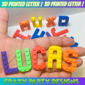 May include: Colorful 3D printed letters spelling "LUCAS" in various colors, including purple, green, red, yellow, and orange. The letters are designed to resemble toy building blocks. The image also includes the text "3D PRINTED LETTER !" and "CRAZY PARTY DESIGNS".