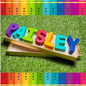 Puede incluir: Un nombre colorido deletreado en letras grandes y gruesas hechas de cera. Las letras están dispuestas en una caja con un borde dorado. Las letras deletrean el nombre "PAISLEY".