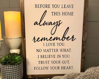 May include: A framed wooden sign with the text "BEFORE YOU LEAVE THIS HOME always remember I LOVE YOU. NO MATTER WHAT. I BELIEVE IN YOU. TRUST YOUR GUT. FOLLOW YOUR HEART." A candle and a potted plant are in the foreground.