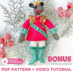May include: A felt mouse dressed as a nutcracker soldier. The mouse is wearing a red and white uniform with gold trim and green boots. The mouse is holding a small sword. The background is a snowy white with green branches and red berries.