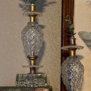 May include: Two clear glass candle holders with gold metal accents and floral accents. The candle holders are on a stack of old books.