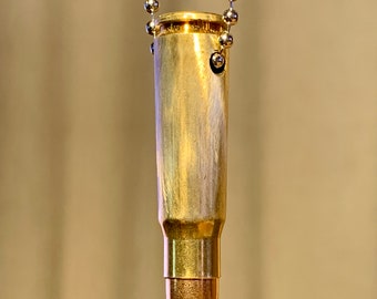 Può includere: Un ciondolo a forma di bossolo di proiettile dorato su una catena d'argento. Il bossolo di proiettile è lucido e ha una finitura lucida. La catena è fatta di piccoli anelli rotondi.