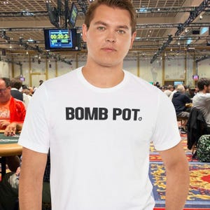 Puede incluir: Camiseta blanca de cuello redondo con el texto "BOMB POT." en letras negras. La camiseta la lleva una persona en un torneo de póquer. Un reloj digital muestra la hora.