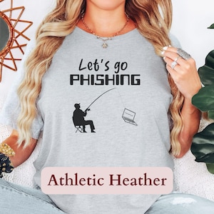May include: Light gray athletic heather t-shirt with the phrase "Let's go PHISHING" in black. A graphic shows a person fishing with a laptop as the bait. The text "Athletic Heather" is below the graphic.
