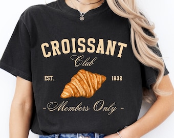 May include: Black t-shirt with a graphic of a croissant and the text "Croissant Club Est. 1832 Members Only".