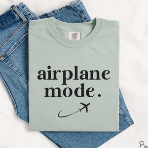 Op de afbeelding: Een lichtgroen t-shirt met de tekst "airplane mode." en een kleine vliegtuigafbeelding.