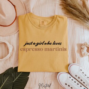 May include: A yellow t-shirt with the text "just a girl who loves espresso martinis" printed on it in black and brown lettering.