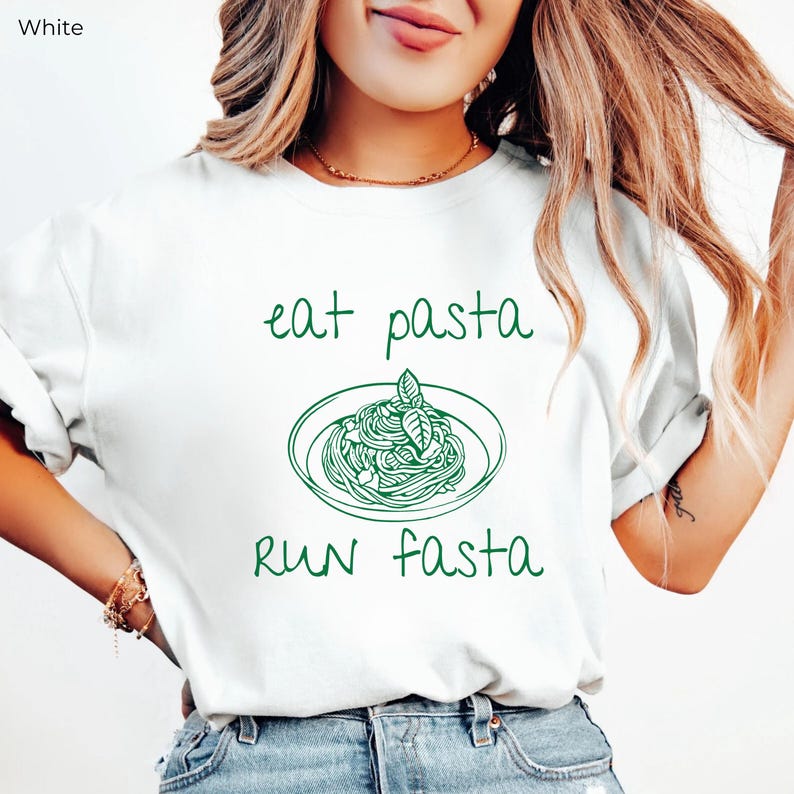 Puede incluir: Camiseta blanca con texto verde que dice "eat pasta run fasta" y un dibujo de un plato de espaguetis con una hoja de albahaca en la parte superior.