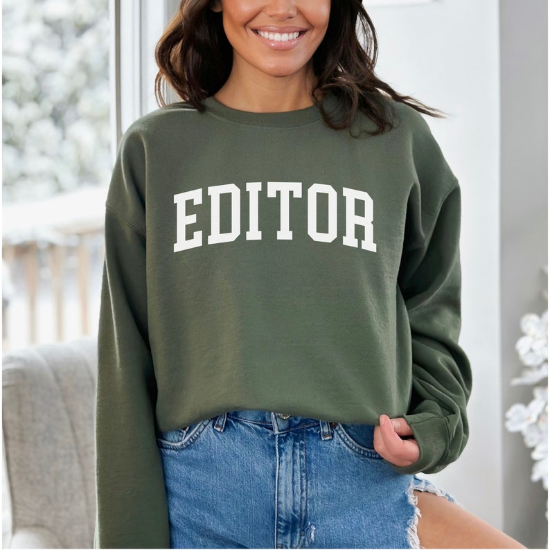 Pode incluir: Uma camisa de moletom verde com a palavra "EDITOR" impressa em branco na frente.