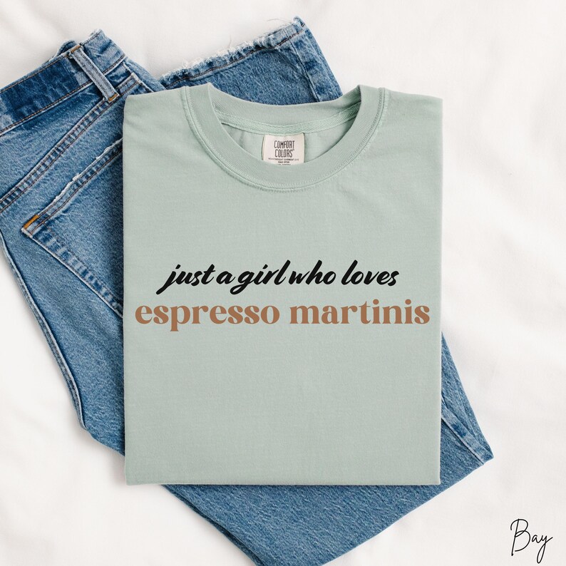 May include: A light green t-shirt with the text "just a girl who loves espresso martinis" in black and brown lettering.