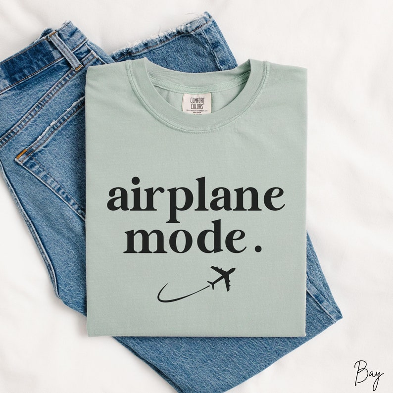 Op de afbeelding: Een lichtgroen t-shirt met de tekst "airplane mode." en een kleine vliegtuigafbeelding.