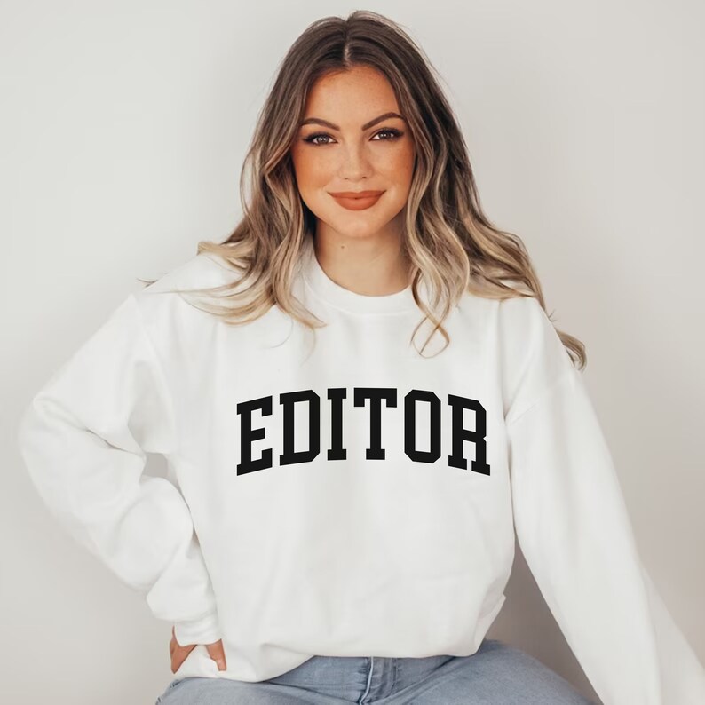 Pode incluir: Camisola branca com texto preto que diz "EDITOR" em uma fonte de estilo universit&aacute;rio.
