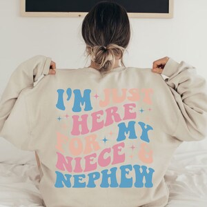 Pode incluir: Camisola bege com o texto "I'M JUST HERE FOR MY NIECE & NEPHEW" em letras azuis, rosa e p&ecirc;ssego. O texto tem uma fonte retro ondulada com detalhes de estrelas. A camisola &eacute; de cor neutra.