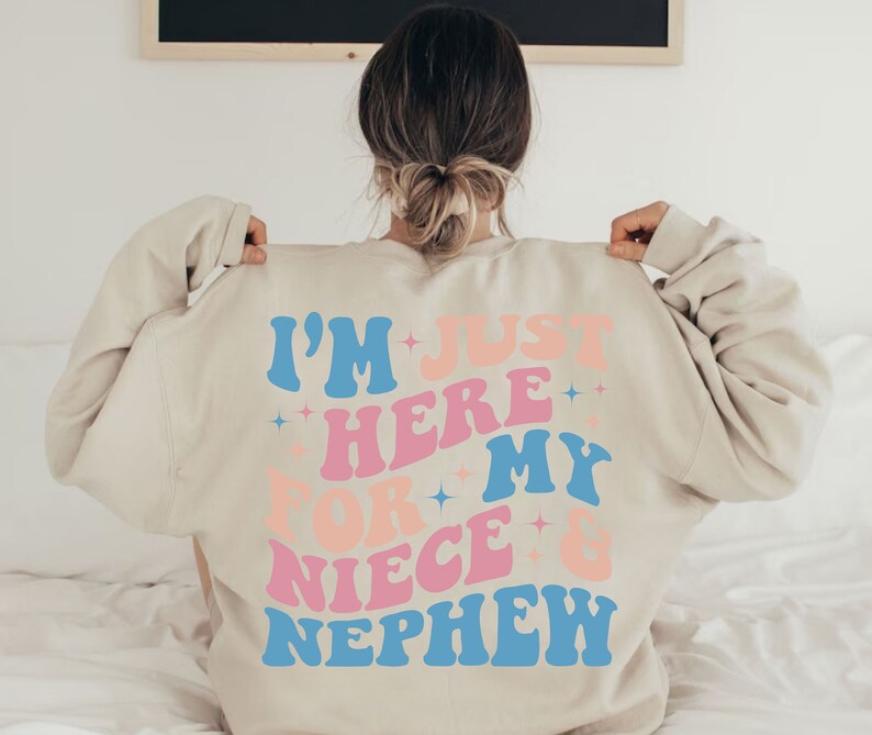 Pode incluir: Camisola bege com o texto "I'M JUST HERE FOR MY NIECE & NEPHEW" em letras azuis, rosa e p&ecirc;ssego. O texto tem uma fonte retro ondulada com detalhes de estrelas. A camisola &eacute; de cor neutra.