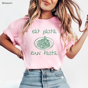 Puede incluir: Camiseta rosa con un gr&aacute;fico verde de un plato de pasta y el texto "eat pasta run fasta".