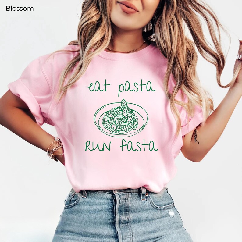 Puede incluir: Camiseta rosa con un gr&aacute;fico verde de un plato de pasta y el texto "eat pasta run fasta".