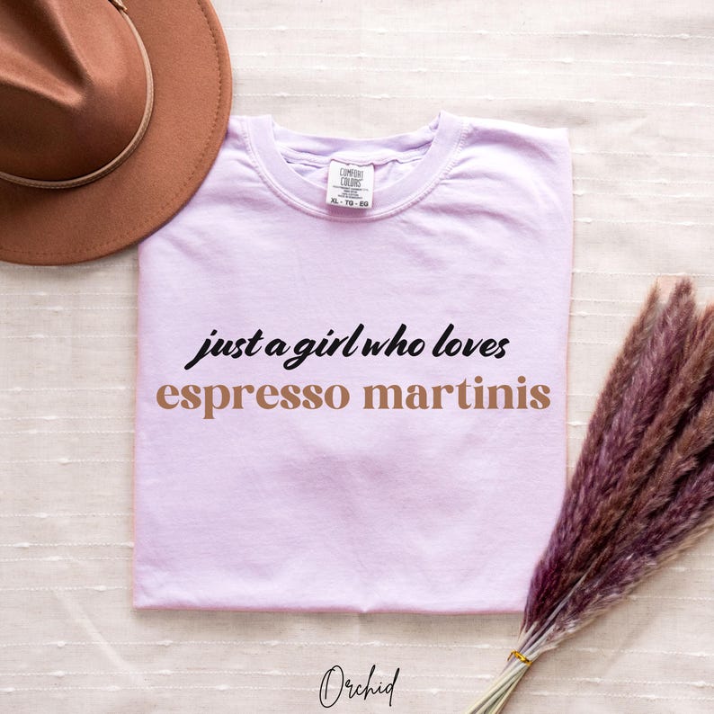 May include: A lavender t-shirt with the text "just a girl who loves espresso martinis" in black and brown lettering.