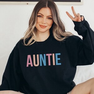 Pode incluir: Camisola preta com a palavra "AUNTIE" impressa em letras rosa, p&ecirc;ssego, azul e turquesa. A camisola &eacute; de estilo casual, ideal para um look di&aacute;rio.