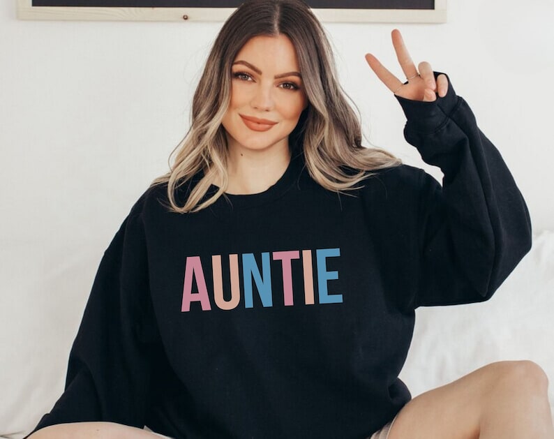 Pode incluir: Camisola preta com a palavra "AUNTIE" impressa em letras rosa, p&ecirc;ssego, azul e turquesa. A camisola &eacute; de estilo casual, ideal para um look di&aacute;rio.