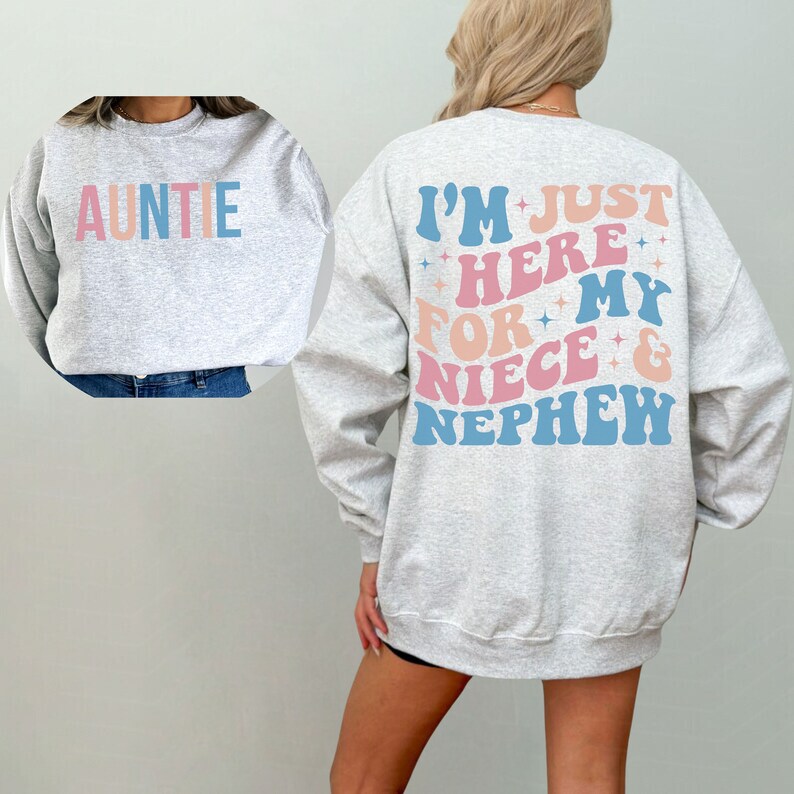Pode incluir: Um moletom cinza claro com a palavra "AUNTIE" em cores pastel na frente. A parte de tr&aacute;s do moletom diz "I'M JUST HERE FOR MY NIECE & NEPHEW" em uma fonte retr&ocirc; com estrelas.