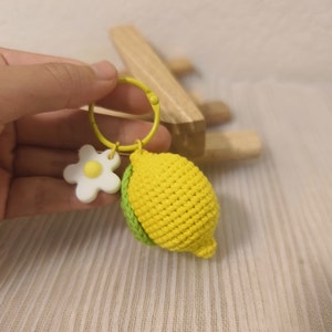 May include: A yellow crocheted lemon keychain with a green crocheted leaf and a white flower charm.