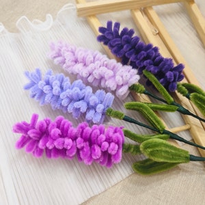 May include: Four artificial lavender flower stems with green leaves. The stems are made of pipe cleaners and the flowers are made of fuzzy yarn. The flowers are in shades of purple, pink, and light blue.