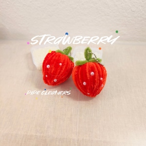 May include: Two red felt strawberry ornaments with green pipe cleaner stems and white pearl accents. The text "STRAWBERRY PIPE CLEANERS" is visible in the image.