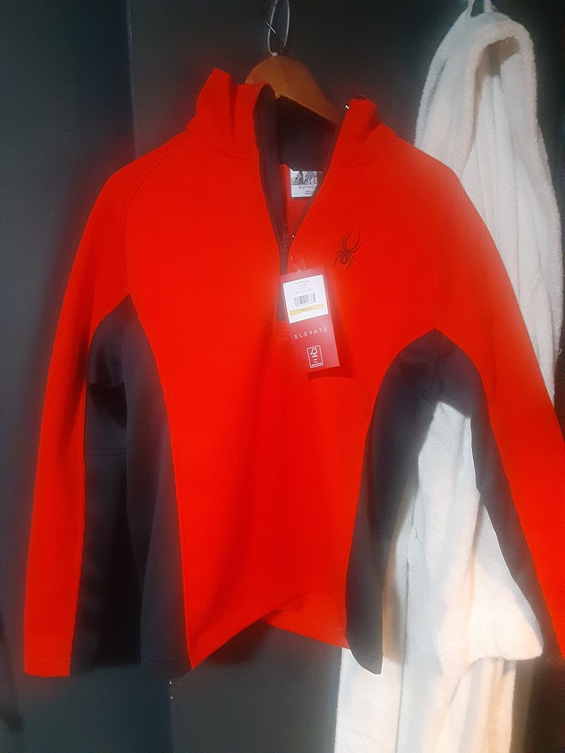 Pode incluir: Camisola de moletom vermelha e preta com capuz, z&iacute;per e um logotipo de aranha. A etiqueta diz "Elevate".