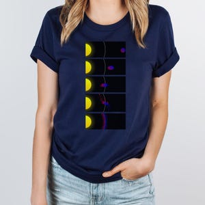 Op de afbeelding: Een marineblauw t-shirt met een afbeelding van een gele zon en een paarse en blauwe planeet. De afbeelding toont de planeet in een reeks fasen rond de zon.