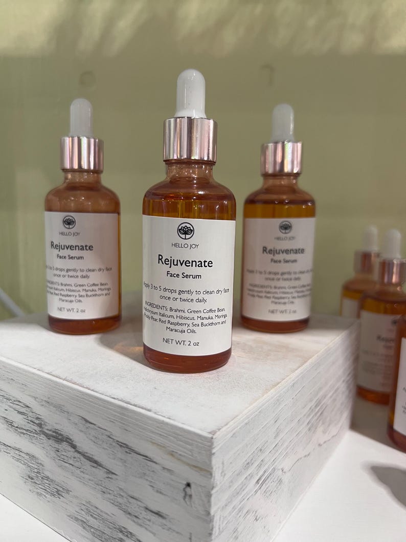 May include: Three amber glass bottles of Hello Joy Rejuvenate Face Serum with white labels and rose gold droppers. The labels list ingredients and usage instructions. Each bottle contains 2 oz of product.