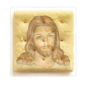 Peut inclure: Un craquant carré avec une image de Jésus-Christ dessus. Le craquant est brun clair et a une surface légèrement texturée.