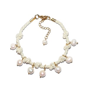 Op de afbeelding: Een wit touw armband met gouden accenten en parel bedels. De armband heeft een geknoopt ontwerp en is versierd met meerdere parels.