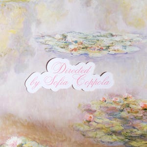 May include: A white ceramic mug with a black handle and the text "But First, Coffee" in a bold, black font. The mug is set against a blurred background, suggesting a cozy setting.