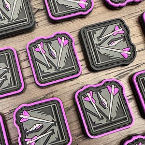 May include: A set of nine black and gray tactical patches with a pink border. Each patch features a stylized image of three arrows hitting a target.