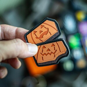 Puede incluir: Dos parches de Halloween de color naranja y negro con un diseño de cara de calabaza. Los parches están hechos de un material suave y texturizado.