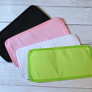 May include: Four rectangular, padded fabric items in black, pink, white, and green. The items are arranged diagonally, with the black one on top. Each item has a contrasting border, and they are likely baby changing pads or similar.