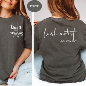 May include: Pepper-colored t-shirt with white text. The front of the shirt says "lashes make everything better". The back of the shirt says "lash artist" with "@CUSTOM TEXT" below. The shirt is a comfortable, casual style.