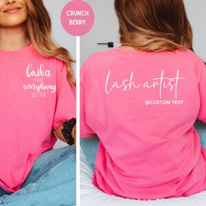 May include: A bright pink t-shirt with white text on the front that reads "lashes make everything better." The back of the shirt says "lash artist" with a space for custom text. The shirt is a loose fit.