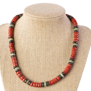 May include: A necklace made of red, black, and green wooden beads. The necklace is on a fabric-covered mannequin.