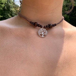 May include: A brown cord choker necklace with brown wooden beads and a silver tree of life pendant.