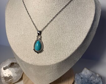 May include: A silver chain necklace with a turquoise teardrop pendant. The pendant has a silver filigree design around the stone.